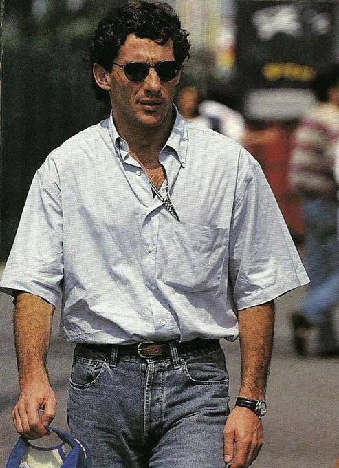 The image features a man walking down a street, wearing a white shirt and blue jeans with sunglasses on his head. He has a blue bag over one shoulder and appears to be carrying a camera around his neck. The caption "That's aura" suggests that he is capturing the essence of the moment or atmosphere in the scene.