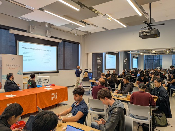An audience attends a Momentum (by Pi Network) event in a large room, with a presenter speaking in front of a slide titled 'An open marketplace for the world's compute.'