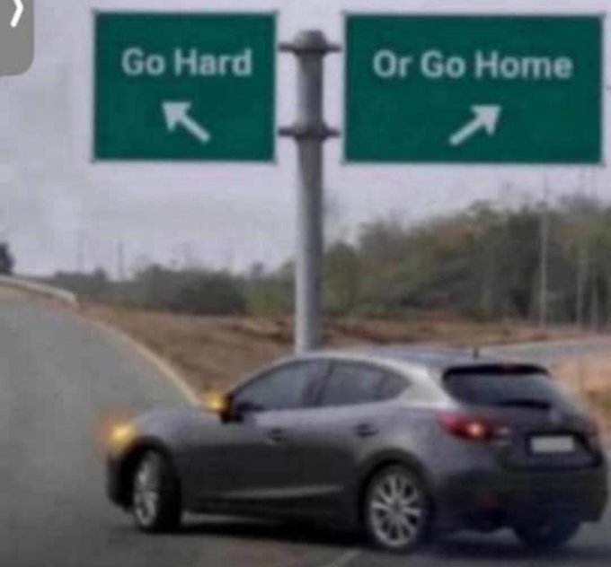 A silver car is shown veering left on a highway toward a green road sign reading "Go Hard" (with an arrow pointing left), while ignoring the right sign reading "Or Go Home" (with an arrow pointing right) — perfectly illustrating the "we're going hard, lock in" mindset of pushing forward instead of giving up.