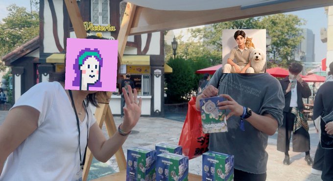 Two friends pose at a "Victoria" branded booth, holding plush red panda toys and boxes of dog biscuits, with 0G promotional merchandise visible. Their faces are covered with pixel art and a photo overlay as they celebrate winning prizes from the 0G Labs event.