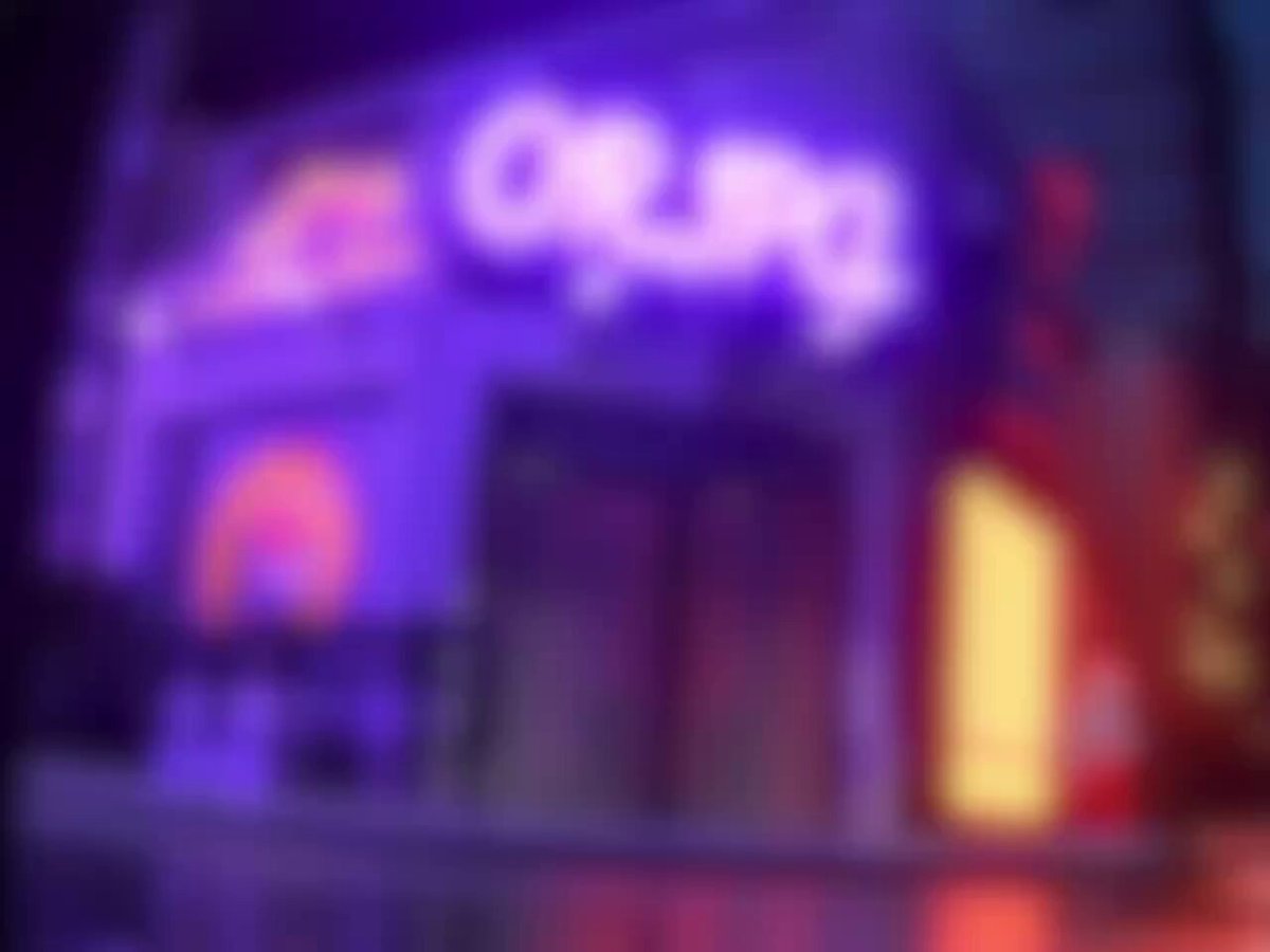 The image features a neon sign for a store called "Crap" that has been turned into a neon billboard by the company. The sign displays the word "Crap" in purple letters against a blue background, creating an eye-catching display. The neon billboard is located on a street corner and appears to be part of a larger advertising campaign or promotional event for the store.