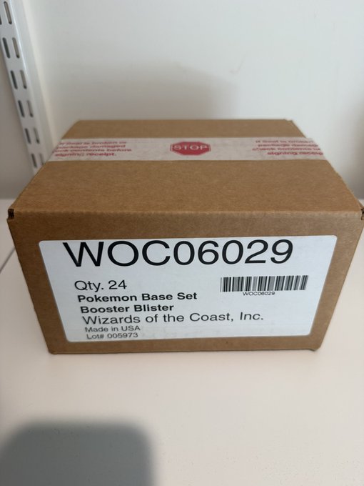 A sealed cardboard case labeled "WOC06029" containing 24 Pokémon Base Set Booster Blister packs from Wizards of the Coast, made in USA, advertised for sale at $60,000 OBO.