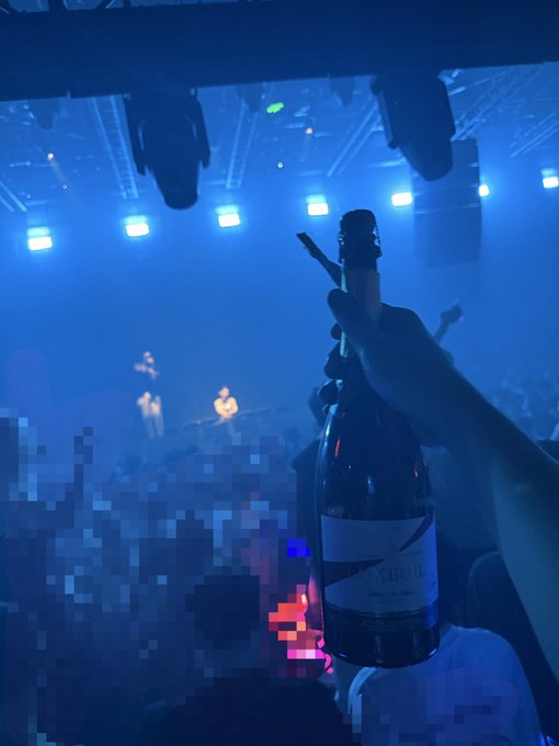 A hand raises a bottle of Grey Goose champagne in celebration at a concert, with blue stage lighting and performers visible in the background. The "To the Mooooooon" caption pairs with the bottle as a celebratory toast to success or achievement.