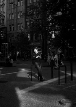 Black-and-white photograph of a person in motion leaning against a pole on a city street, with 'ART DESIGN' signage visible on a building in the background.