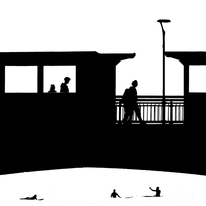 A high-contrast black-and-white silhouette image showing people on a balcony, in windows, and figures on a beach below.