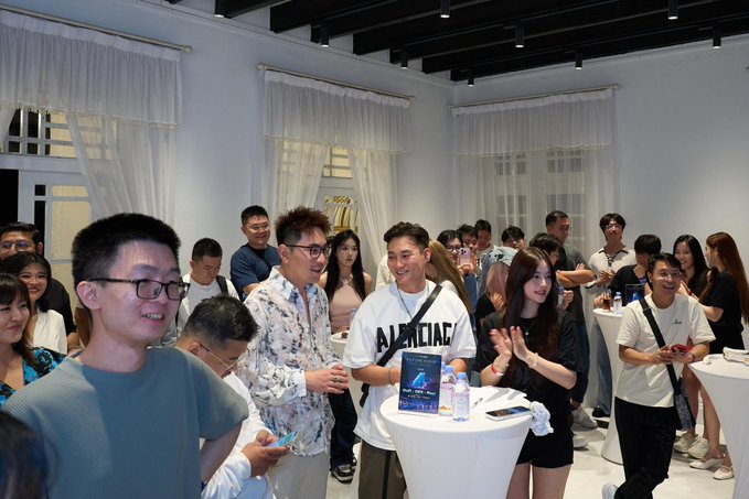 A group of people gather at an indoor social event with high ceilings, curtains, and white cocktail tables, where attendees are mingling and holding drinks.