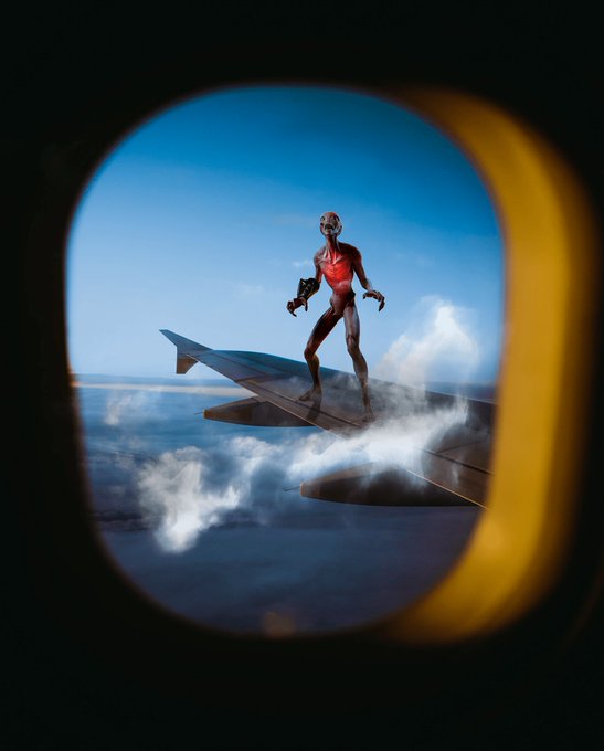 The image features an alien standing on top of an airplane wing, looking out through an open window. The photo has a creative twist with the presence of clouds and a cartoonish appearance that adds a sense of whimsy to the scene. The caption provided seems unrelated to the main subject matter but is included for context or to provide additional information about the image.