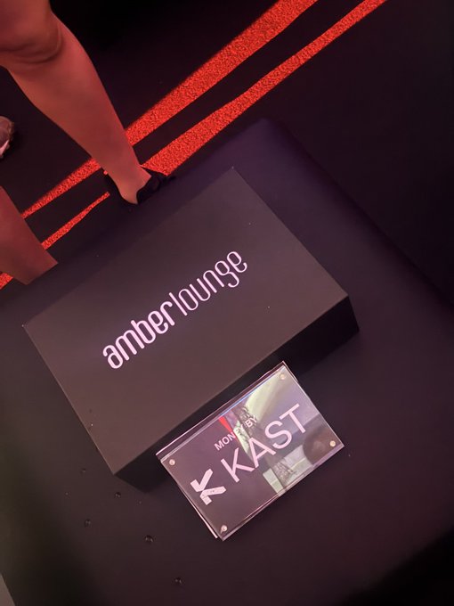 A black "amber·lounge" box sits on a dark carpet accented with red stripes, next to a VIP badge reading "MON..." and "KAST" in bold white letters, complementing the post's praise for @KASTxyz events.