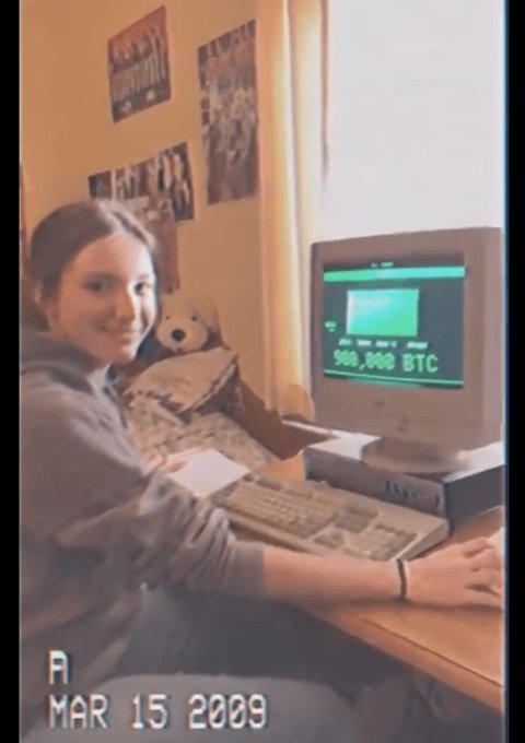 A vintage photo from March 15, 2009 showing a young woman sitting at a desk with an old computer monitor displaying '500,000 BTC'.