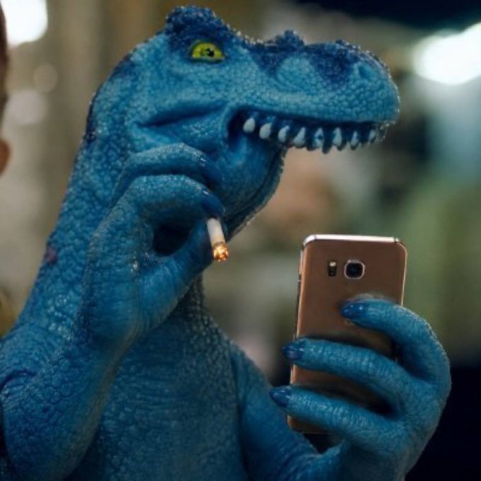 A person dressed in a blue velociraptor costume is looking at a smartphone while smoking a cigarette.