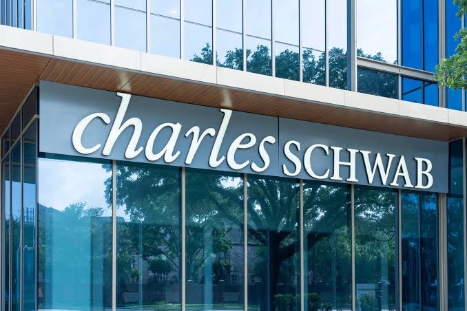 The exterior entrance of a Charles Schwab office building, featuring the company's name in white lettering on a dark sign above glass doors.