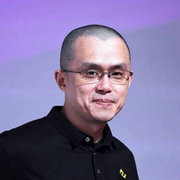 The image features a man wearing glasses with short hair who appears to be smiling for the camera. He is dressed in a black shirt, which contrasts with his short hair. The background of the image is purple, adding a unique touch to the overall composition. There are no texts or other objects present in the image, and the focus remains solely on the man and his facial expression.