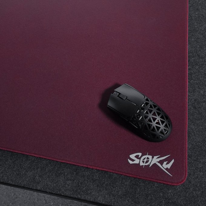 A sleek black gaming mouse with a geometric lattice design rests on a deep burgundy mousepad featuring the "SOKU" logo in stylized white lettering at the corner. The product showcase complements the post's praise for the brand's distinctive visual appeal and standout design in the competitive gaming peripherals market.