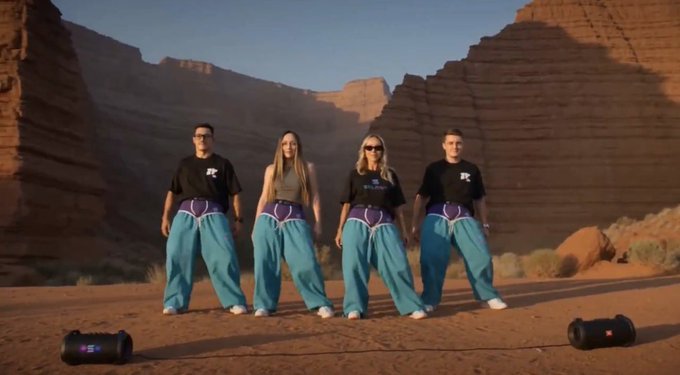 Four people in matching teal and purple outfits with "SF" shirts stand confidently in a desert canyon, flanked by two portable speakers, embodying the Solana brand's creative identity and playful spirit referenced in the post about building a distinctive brand world.
