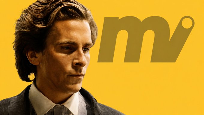A promotional image featuring a man in a suit against a yellow background, with a large stylized "mv" logo next to him.