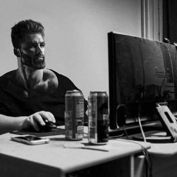 A black-and-white photo shows a man seated at a desk using a computer, with two beverage cans and small electronics in front of him. The image does not visibly reference Alpenglow, Solana, or any other text, numbers, tickers, or names.