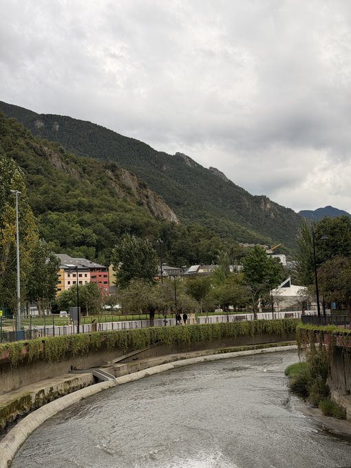 A scenic mountain valley town with a concrete canal/river channel running through it under cloudy skies, with green hills rising dramatically behind modest buildings. The peaceful morning landscape complements the post's "Morning run" caption, showing the runner's route through this picturesque Alpine-style setting before settling back into market analysis.