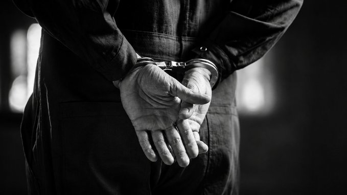 A black and white image of a person's hands cuffed behind their back.
