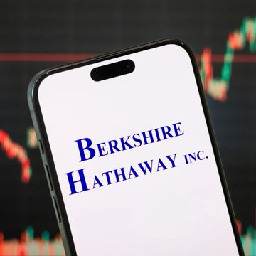 A smartphone displays the Berkshire Hathaway Inc. logo against a background of a stock market chart.