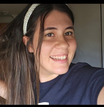 A selfie of a smiling young woman with long dark hair wearing a pearl headband and dark blue shirt.