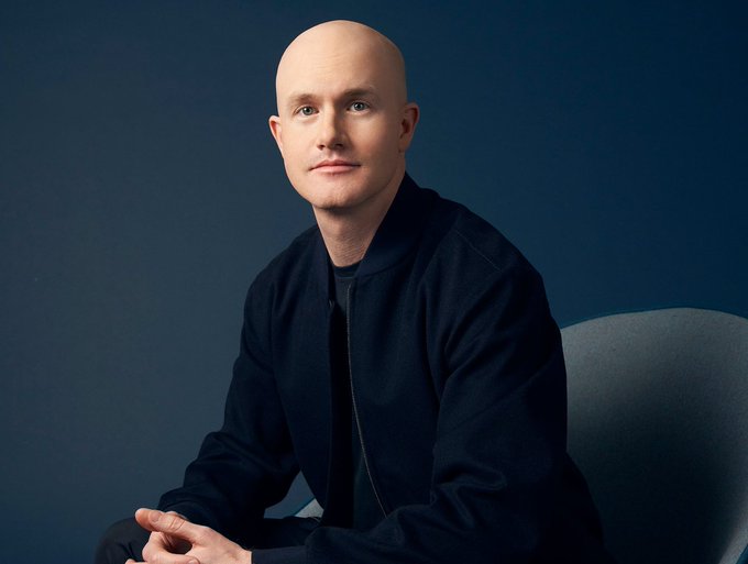 The image shows a bald man wearing a dark navy zip-up jacket, seated and looking toward the camera against a deep blue backdrop. Based on the accompanying post about Coinbase and stock market rallies, this appears to be Coinbase CEO Brian Armstrong, who is pictured here likely during an interview or professional photo shoot where he discussed crypto and market growth.