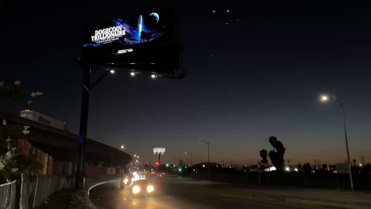 The image features a billboard with a large blue screen displaying an advertisement, possibly related to the popular YouTuber, Maximus. The billboard is located at an intersection of two streets, surrounded by traffic lights and streetlights. There are several cars on the road below the billboard, indicating that it is situated in a busy area. The post also includes text about a new series called "Maximus" and a reference to the YouTuber, Maximus.