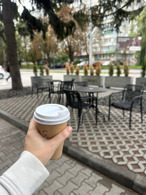 A hand holds a takeaway coffee cup while enjoying a quiet moment at an outdoor café seating area. The relaxed setting perfectly captures the well-deserved coffee break mentioned in the post after a busy morning.