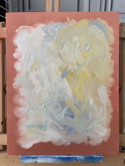 An abstract oil painting on a coral/salmon-colored canvas featuring thick brushstrokes in white, yellow, and light blue tones, displayed on a wooden easel.