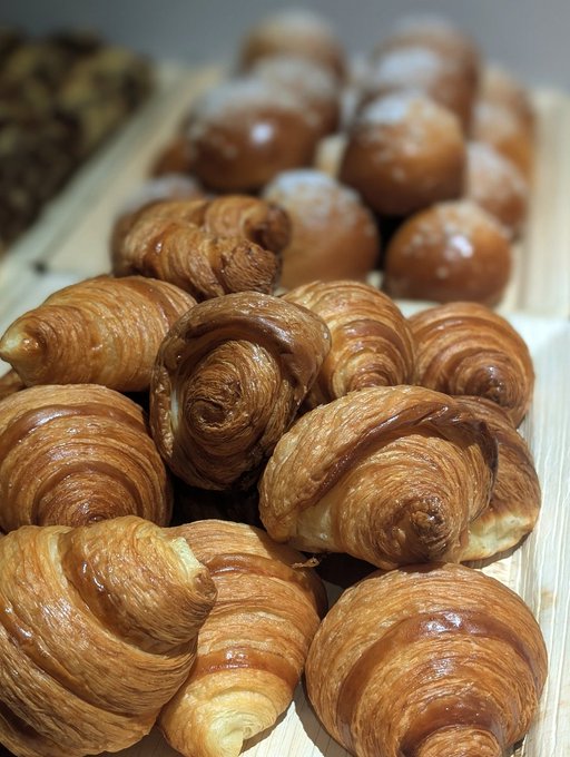 A close-up photograph shows a tray piled high with freshly baked, glossy croissants arranged in neat rows.