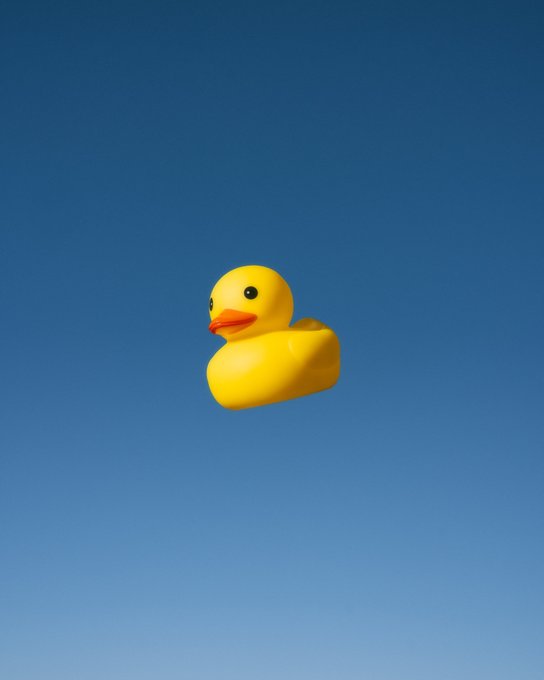 A bright yellow rubber duck floats against a clear blue sky, playfully illustrating the "Rubber Duck" acquisition referenced in the post by @CryptoLeszto.