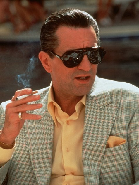 A man in a checkered blazer and sunglasses smokes a cigarette, exuding a retro, stylish vibe reminiscent of classic cinema.
