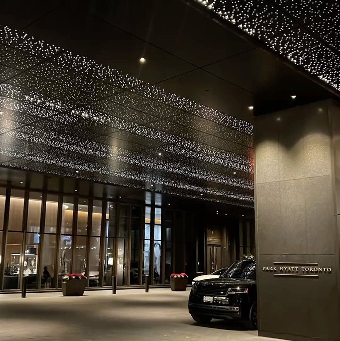 The entrance of the Park Hyatt Toronto is shown at night, featuring a black SUV parked at the porte-cochère under a ceiling installation resembling a starry sky.