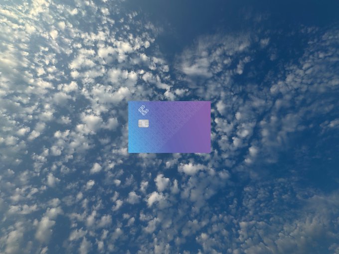 A blue and purple credit card floating against a backdrop of scattered white clouds and blue sky.