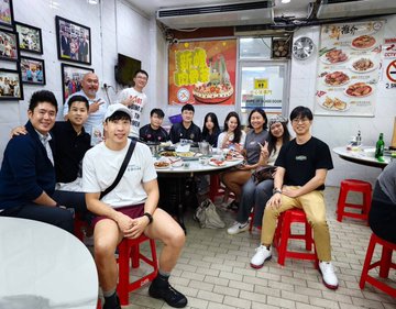 A group photo of about nine people gathered around a round table in a restaurant, posing together with food and drinks visible.