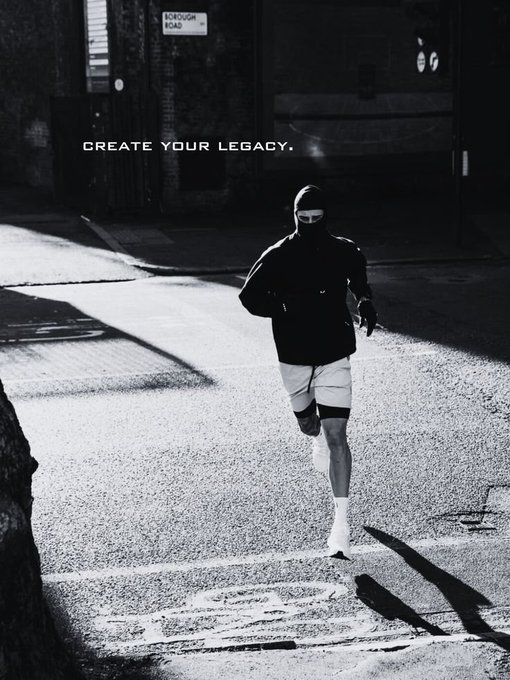 A black and white motivational image showing a person in athletic wear and a face covering running on a city street, with the text 'CREATE YOUR LEGACY.' displayed in the upper left corner.