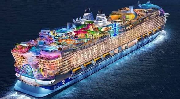 A large, brightly lit cruise ship named 'ICON OF THE SEAS' by Royal Caribbean sails through dark blue waters at night, featuring colorful illuminated decks and a water park.