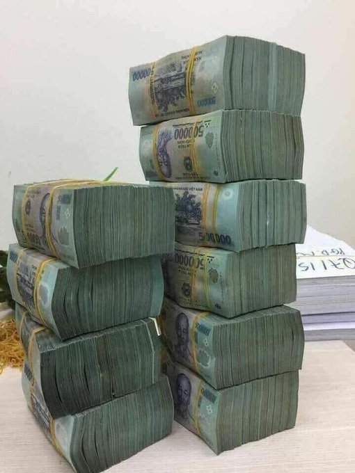 Stacks of banded banknotes appearing to be Venezuelan bolívars (50,000 denomination) piled on a desk, with documents labeled 'DETAILS' visible in the background.
