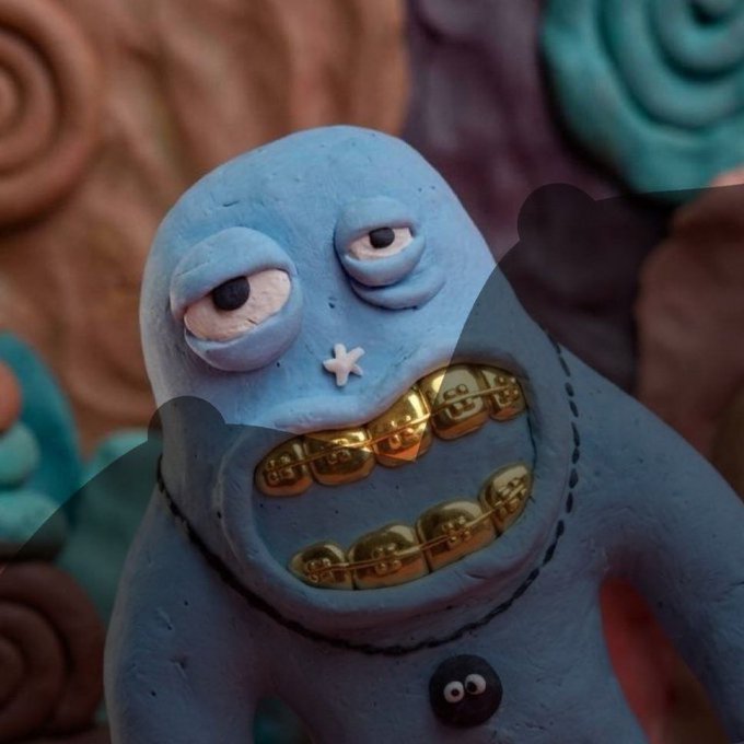 A close-up of a quirky clay or vinyl figurine of a blue monster with droopy eyes, a small 'X' mouth, and a wide grin revealing gold-capped teeth, with colorful spiral shapes in the background.