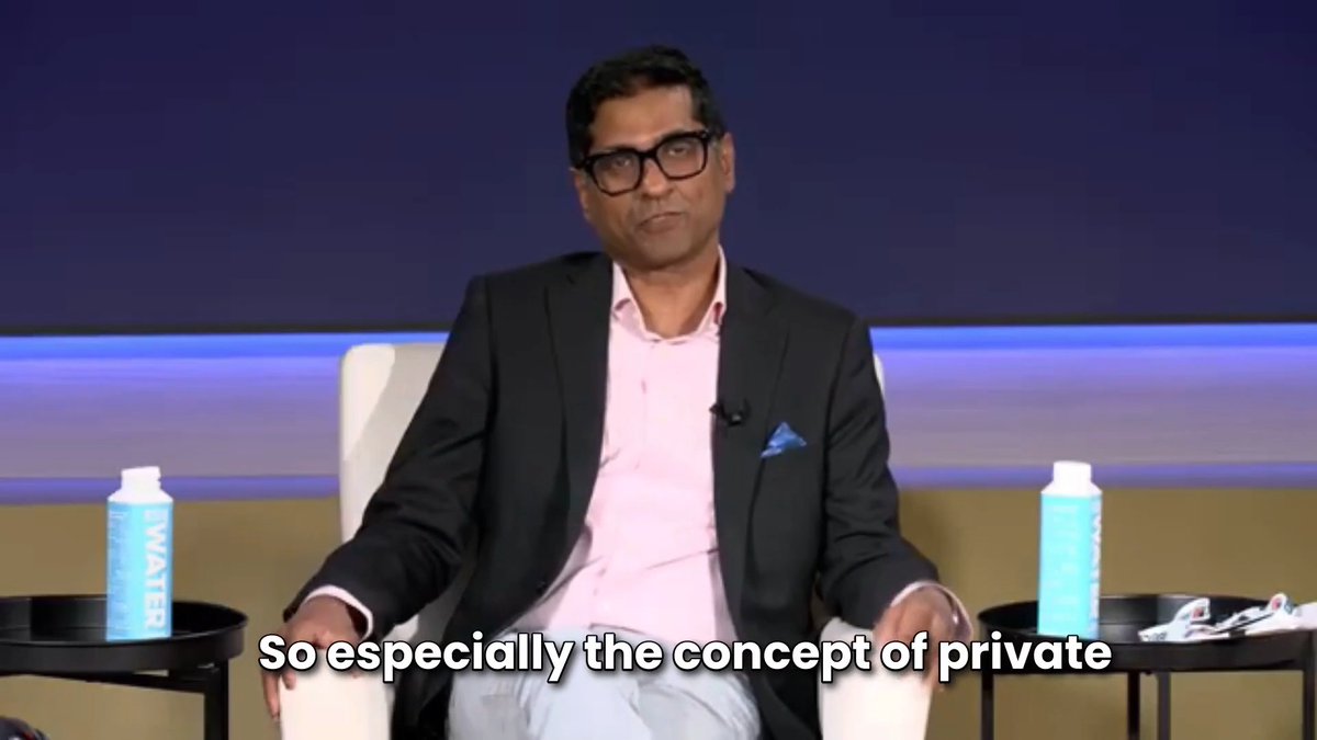 The image shows a man sitting in a chair with his arms crossed, wearing glasses and a suit jacket. He appears to be engaged in a conversation or presentation. The background of the image features two bottles placed next to each other, possibly representing different perspectives on the topic being discussed.