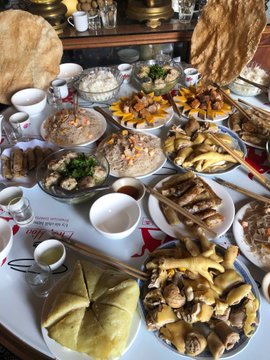 An overhead view of a table laden with numerous small bowls containing various foods, including flatbreads, salads, and other dishes, arranged around chopsticks and condiments.
