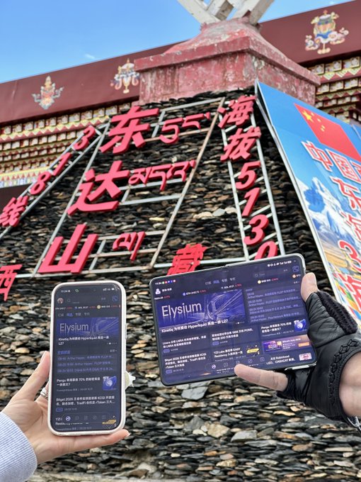Photo of hands holding a phone and tablet displaying the Elysium (永续) cryptocurrency exchange (Apex Vault Perpetual) against a backdrop of train tracks and Chinese/Tibetan script.