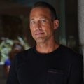 A photograph of Dwayne "The Rock" Johnson wearing a black t-shirt, looking off to the side with a serious expression, set against a blurred background.