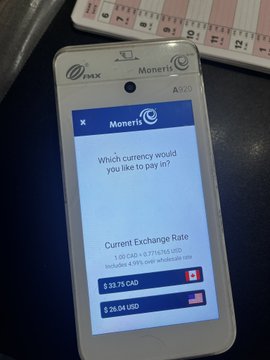 A Moneris payment terminal screen displaying 'Which currency would you like to pay in?' with exchange rates of $33.73 CAD and $25.04 USD available for selection.