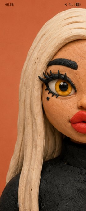 A close-up of a clay-style sculpted figurine with long blonde hair, large yellow eyes, and red lips against an orange background.