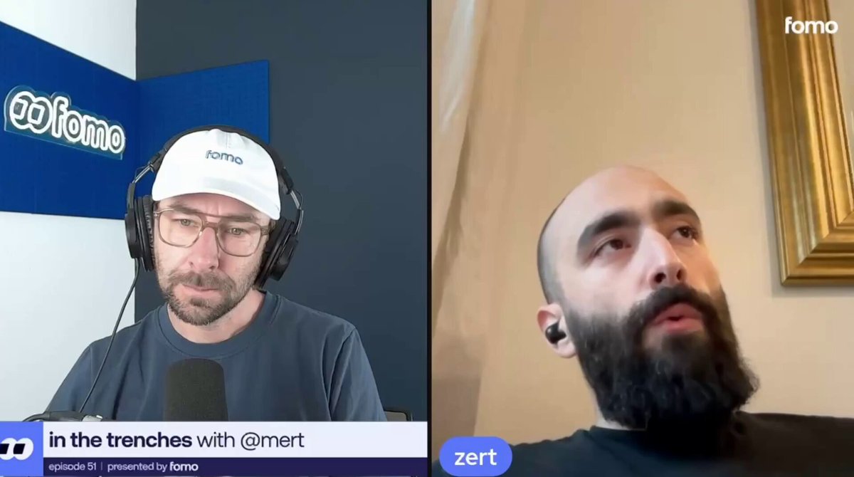 The image shows two men sitting next to each other with microphones in front of them, suggesting they are participating in an online interview or discussion. The man on the left has a beard and is wearing glasses, while the man on the right also has a beard but without glasses. They appear to be engaged in a conversation about physics, as indicated by the post that says "Mert on physics, incentives, and what comes next: ...a network of people who are all trying to build it." The image focuses on their interaction with each other rather than any specific content within the image itself.