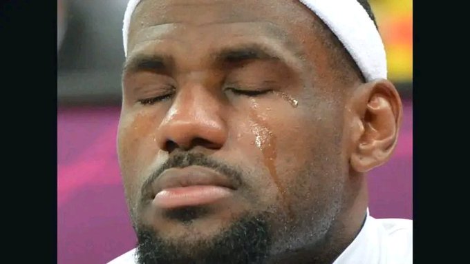 A close-up photograph captures a man, resembling a professional athlete, wearing a white cap with a tear running down his face and his eyes closed.