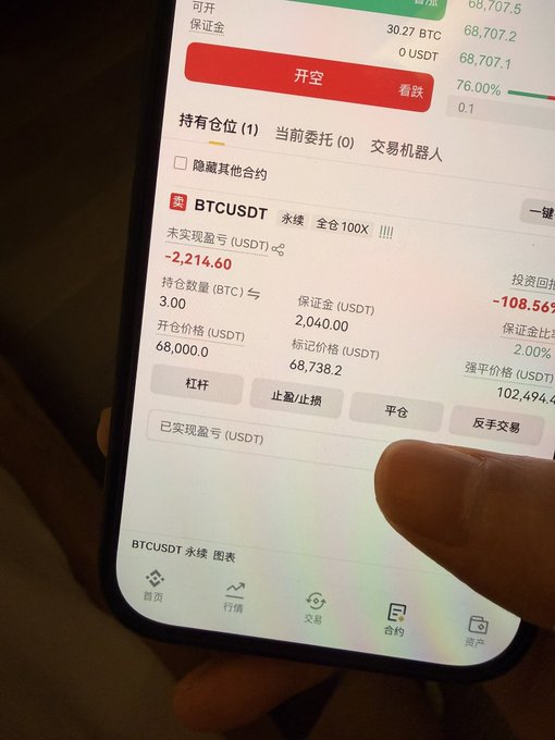 A close-up photo of a smartphone displaying a cryptocurrency trading app showing a short (做空) BTCUSDT perpetual contract position with a 100x leverage, an unrealized profit/loss of -2,214.60 USDT on 3.00 BTC with a margin of 2,040 USDT, while BTC prices hover around 68,000–68,707 USDT—reflecting the poster's patience waiting for Bitcoin to reach their target at the 68k level during a bearish market.
