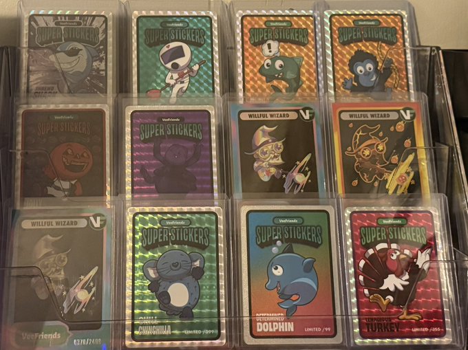 A display case containing collectible 'SuperStickers' cards from Vocaloid and Veefriends, including holographic cards labeled 'SHREKKING SHARK', 'DIFFERENTLY ABLED DOLPHIN LIMITED/99', and 'THANKFUL TURKEY LIMITED/254'.