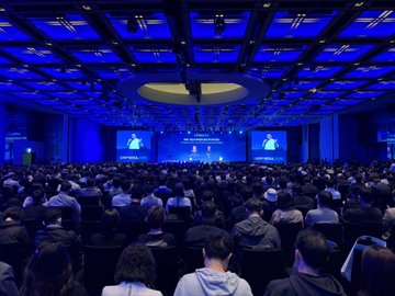 A large conference hall illuminated in blue lighting, filled with attendees seated facing a main stage with screens displaying 'BRICS CHARM', likely the BRICS Summit in Kazan.