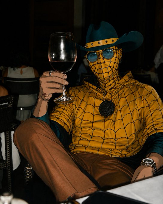 A person dressed in a Spider-Man costume wearing a teal cowboy hat, holding a glass of red wine while sitting at a table.